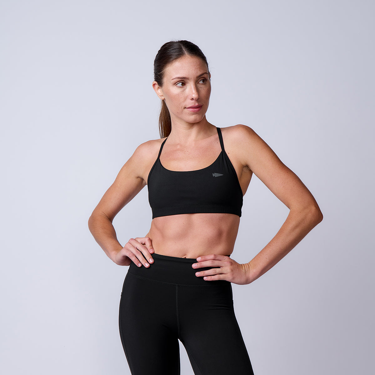Woman wears the Stealth Bra - ToughFlex in black, featuring lightweight support, as she stands with one hand on her hip and gazes aside against a plain background.