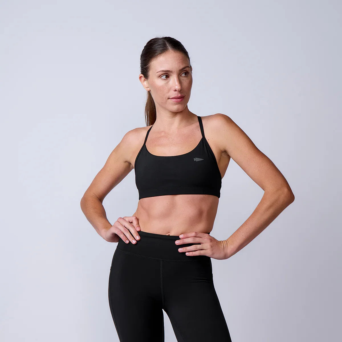 Fit woman wearing black GORUCK sports bra and leggings posing against plain light gray background