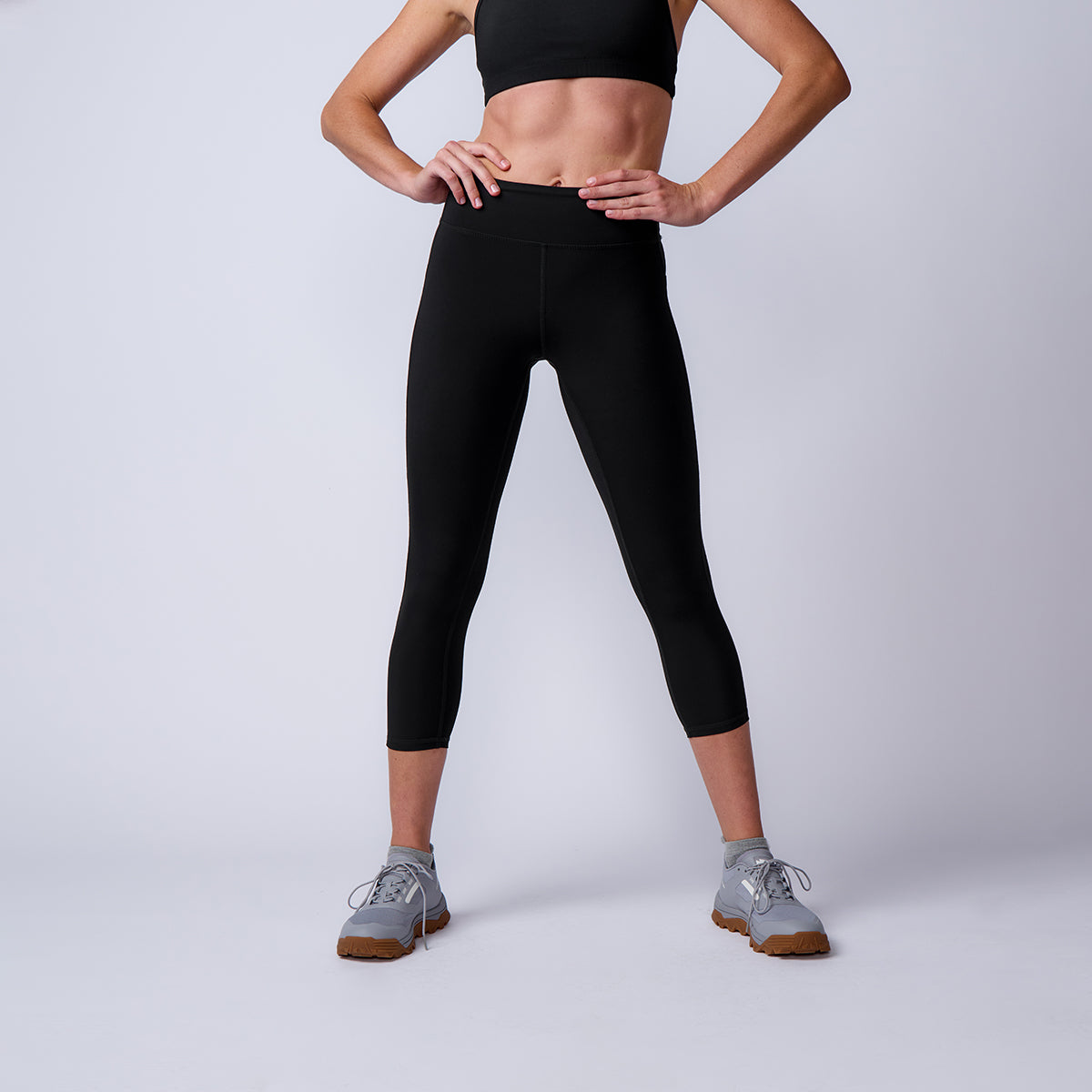 Woman wears Women’s Training Leggings Pocket - ToughFlex in black with a matching sports bra and gray sneakers, standing hands on hips.