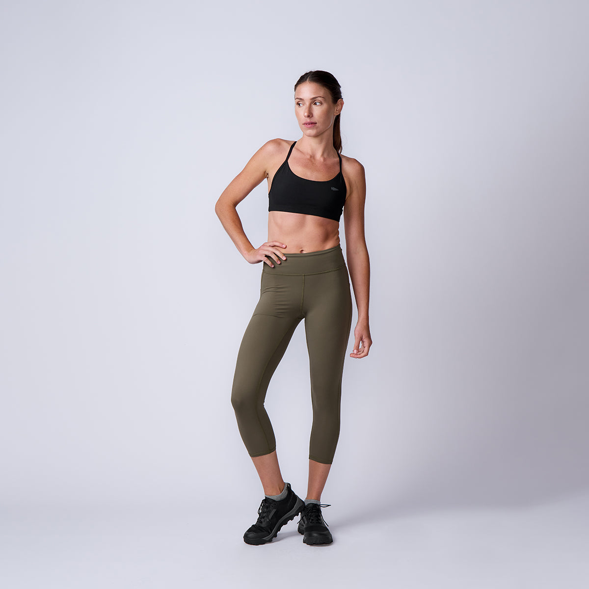Woman in black sports bra, Women’s Training Leggings Pocket - ToughFlex in olive green, and black sneakers poses confidently against a plain light background.