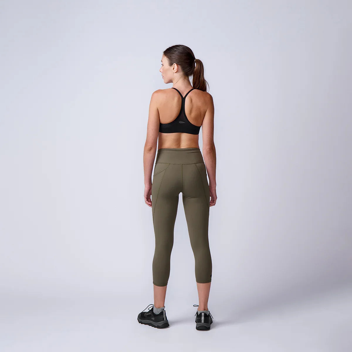 Woman in athletic rucking gear, olive leggings and black sports bra, studio background, GORUCK