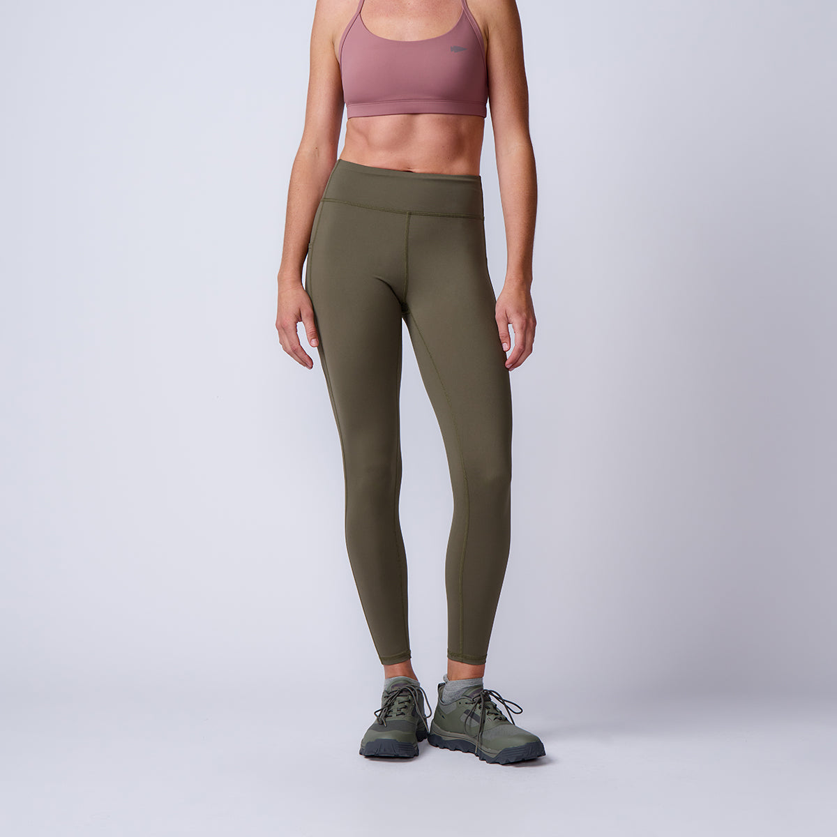 A woman wearing ToughFlex Women’s Training Leggings with pockets in olive, a mauve sports bra, and green sneakers stands against a plain background.