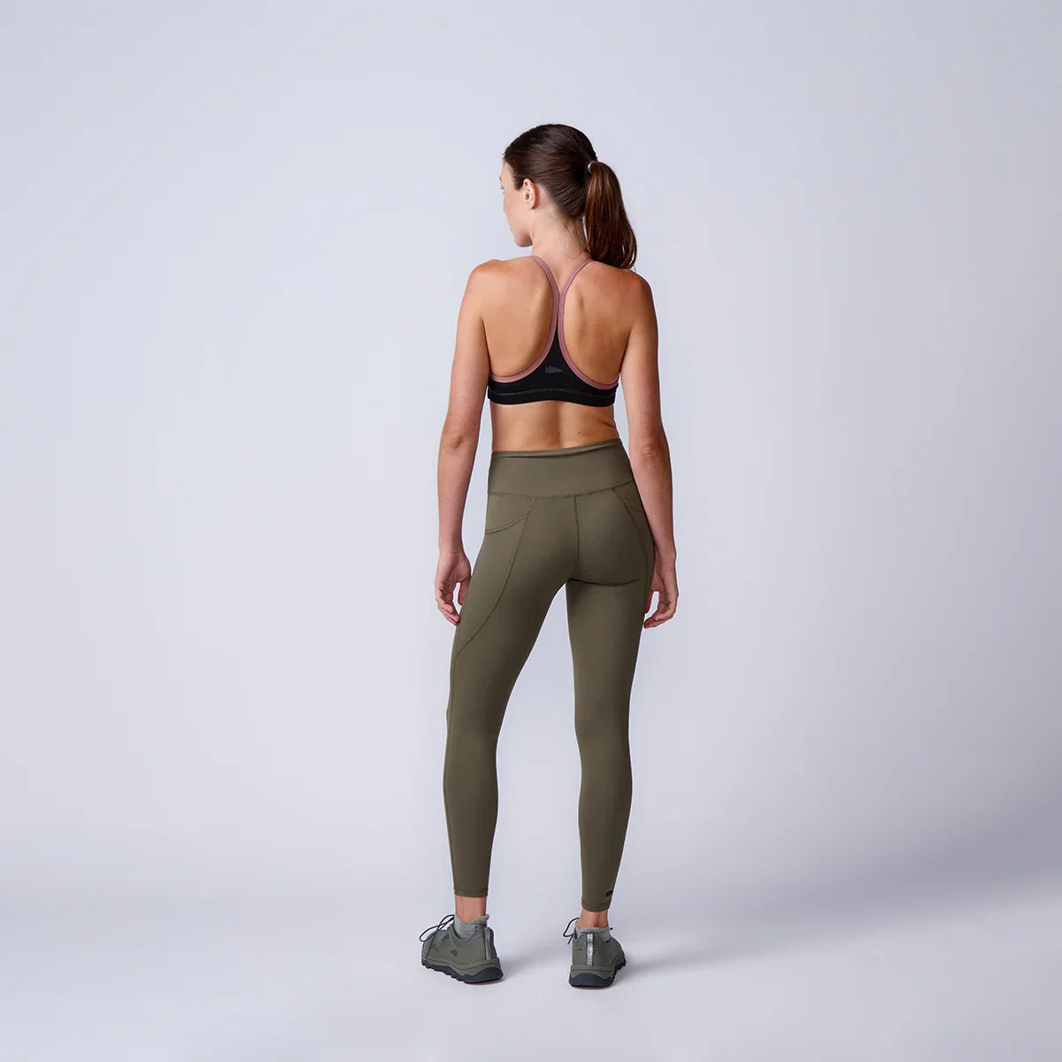 Woman in GORUCK olive green leggings and sports bra standing in studio, back view