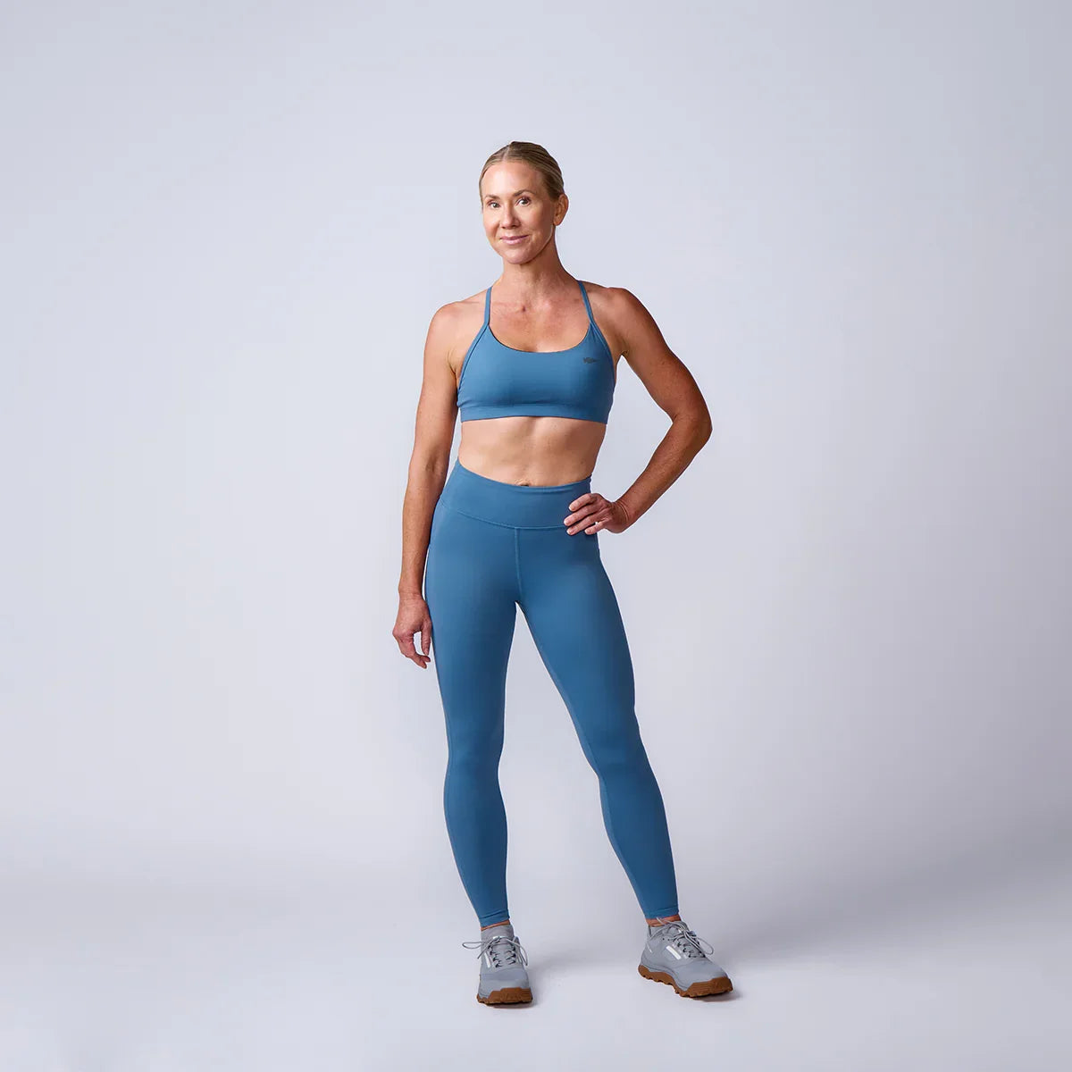 Woman in blue GORUCK athletic wear posing confidently in studio with neutral background