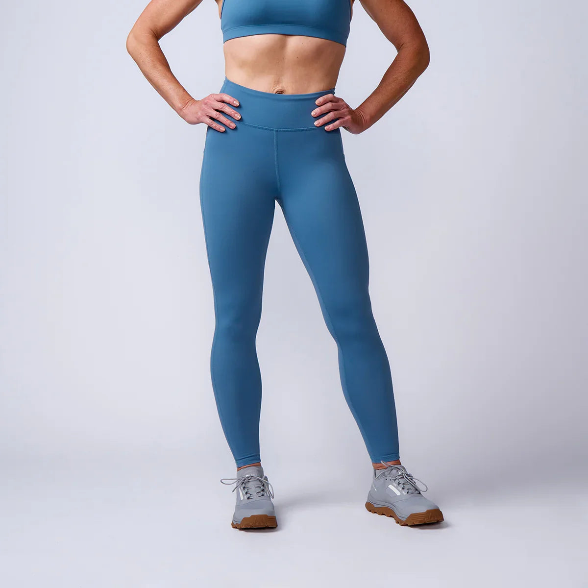 Woman wearing blue GORUCK rucking tights and sneakers in studio setting
