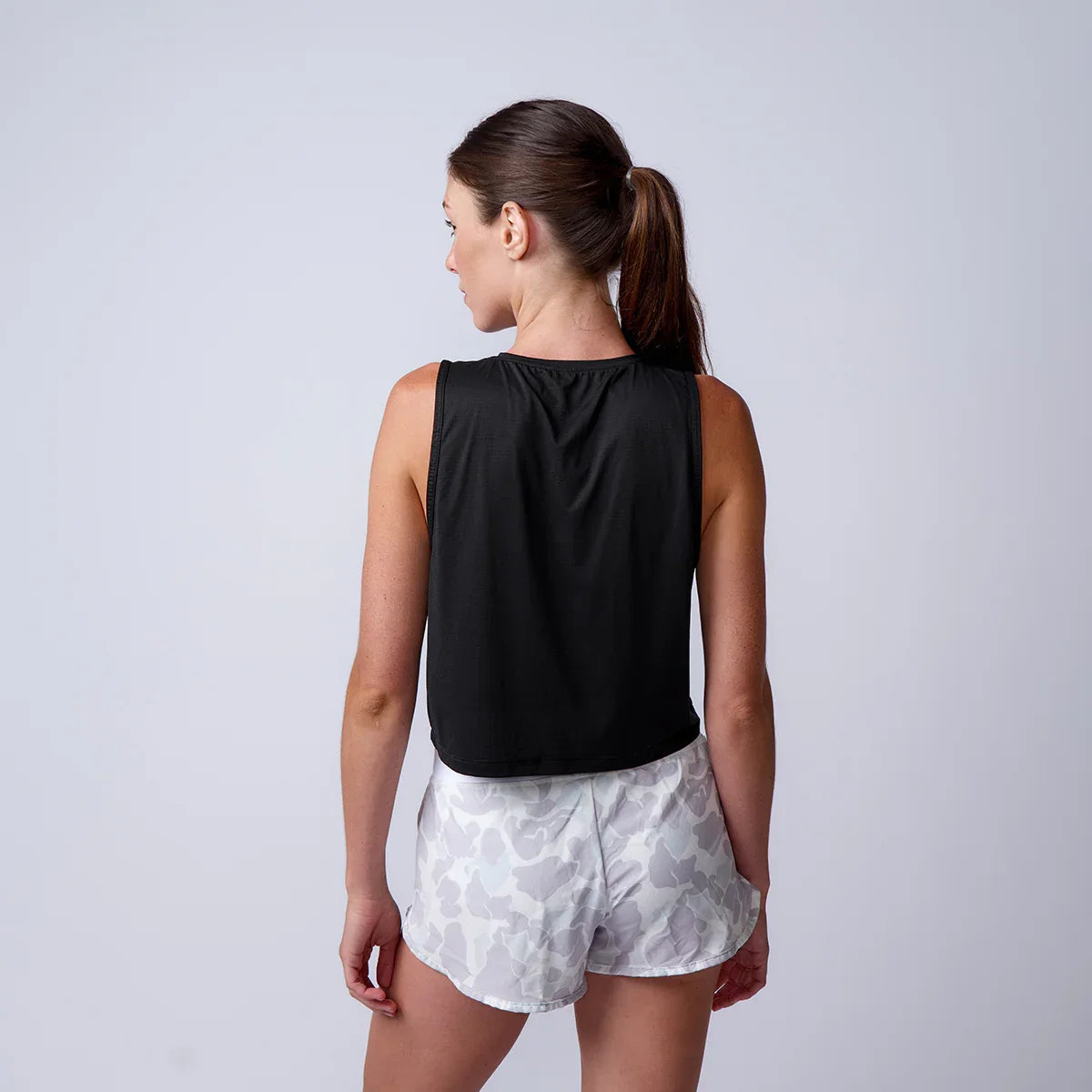 Woman wearing black sleeveless workout tank and light gray camo athletic shorts, standing back view