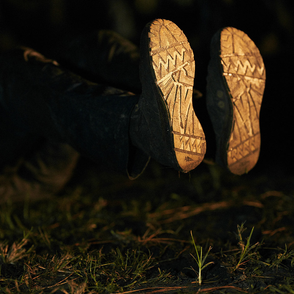A person lying on the ground at night, shown from behind, with illuminated shoe soles visible.
