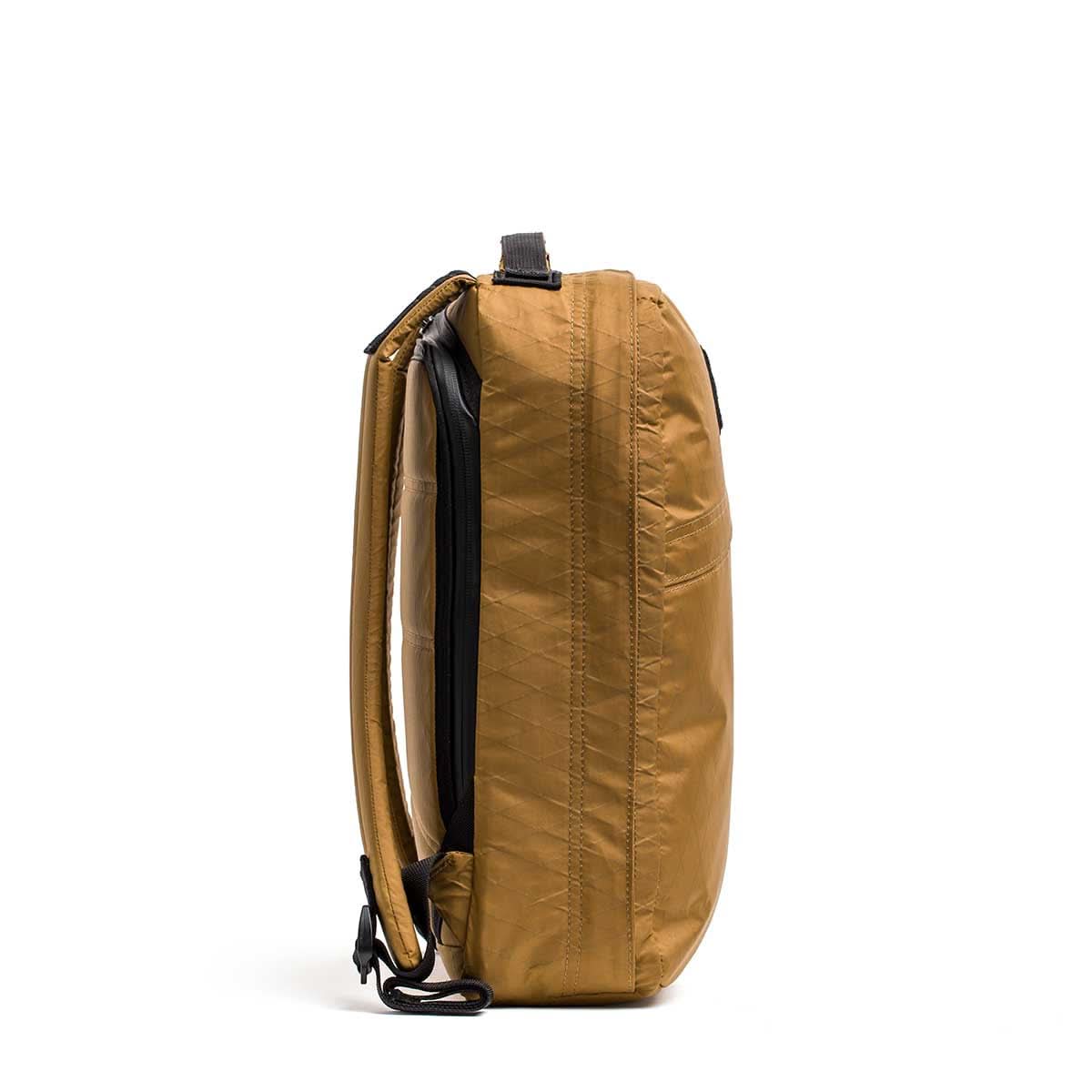The GR0 - X-PAC, a slim, lightweight brown rucksack, stands upright on its side against a white background.