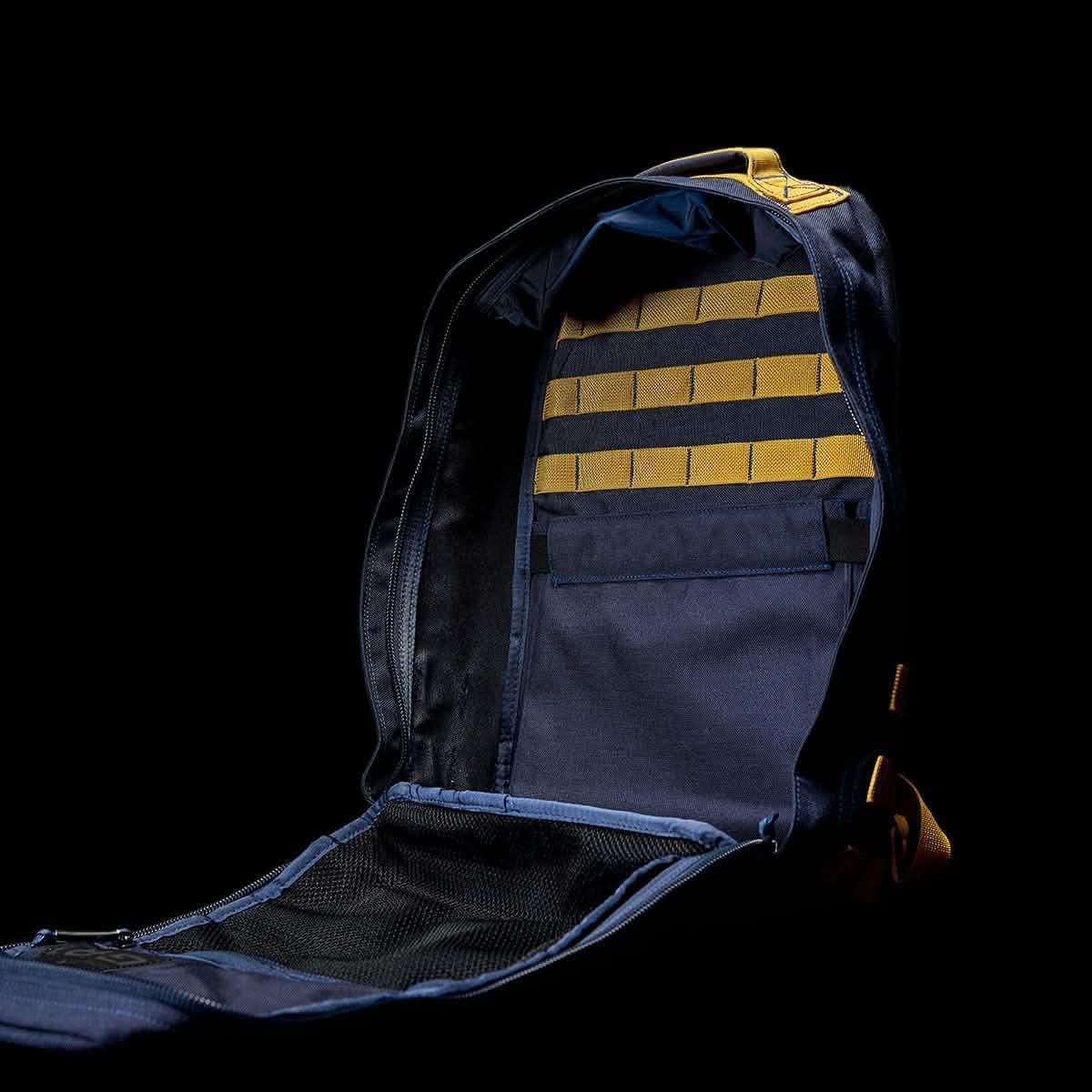 Open navy blue GORUCK backpack displaying interior pockets and yellow MOLLE webbing on a black background