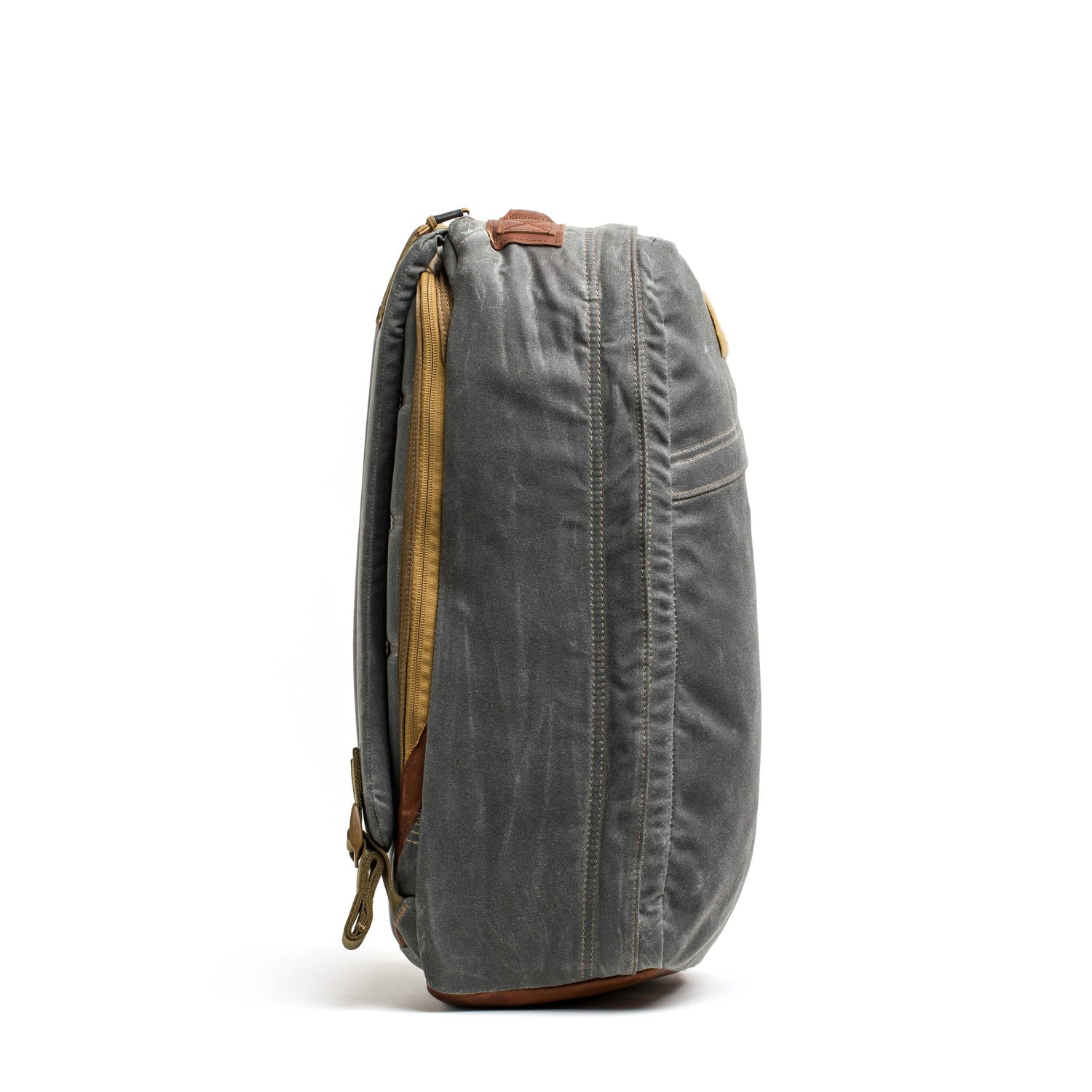 A side view of the GR1 USA - Heritage rucksack by GORUCK, featuring gray waxed canvas with brown leather accents and a zipper. The fabric showcases a rugged texture against the plain white background.