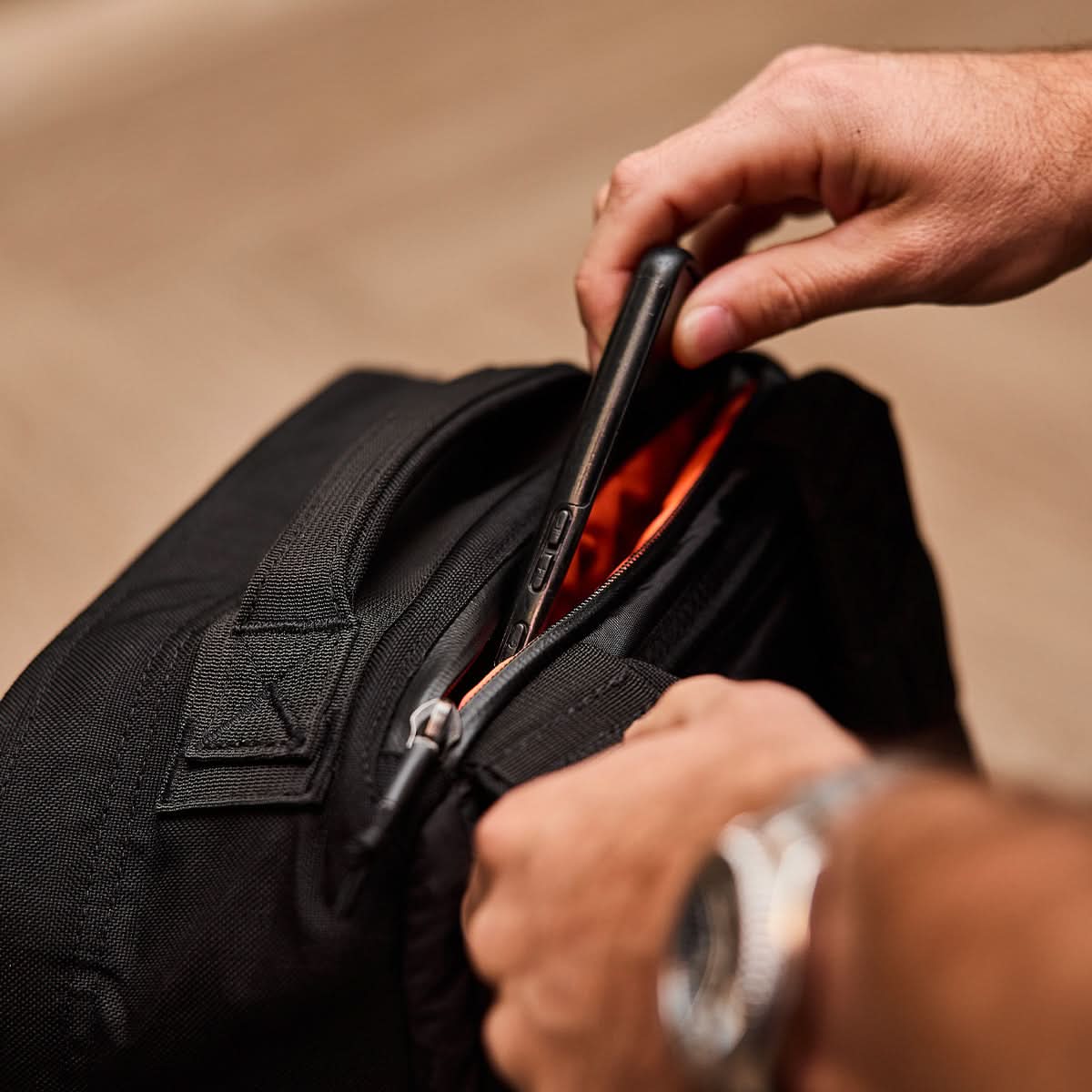 A person places a smartphone into the front pocket of a black GR1 USA - Ballistic Nylon Cordura (The Original Ruck) 210D Back Panel, the ultimate everyday carry rucksack.
