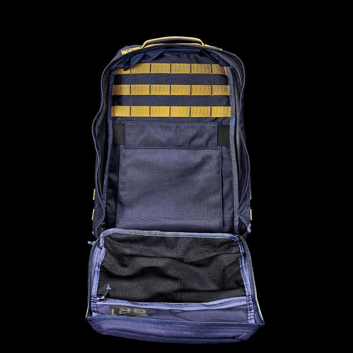 Open navy blue GORUCK backpack showing internal light gold MOLLE webbing and mesh stash pocket