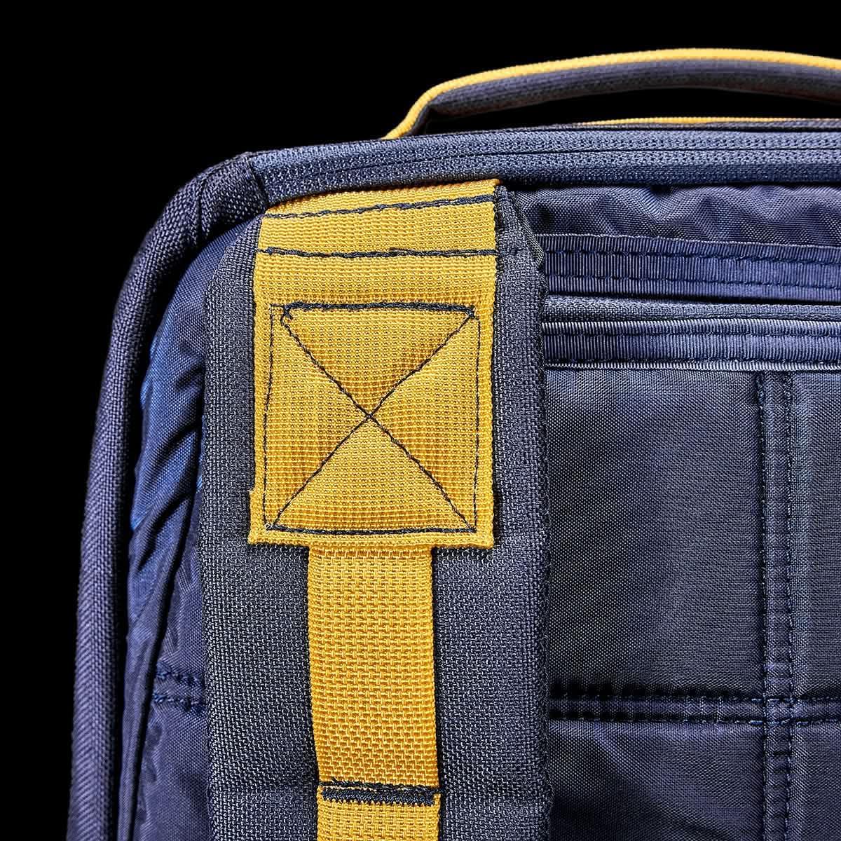 Close-up of navy blue GORUCK backpack with durable yellow strap and reinforced stitching detail