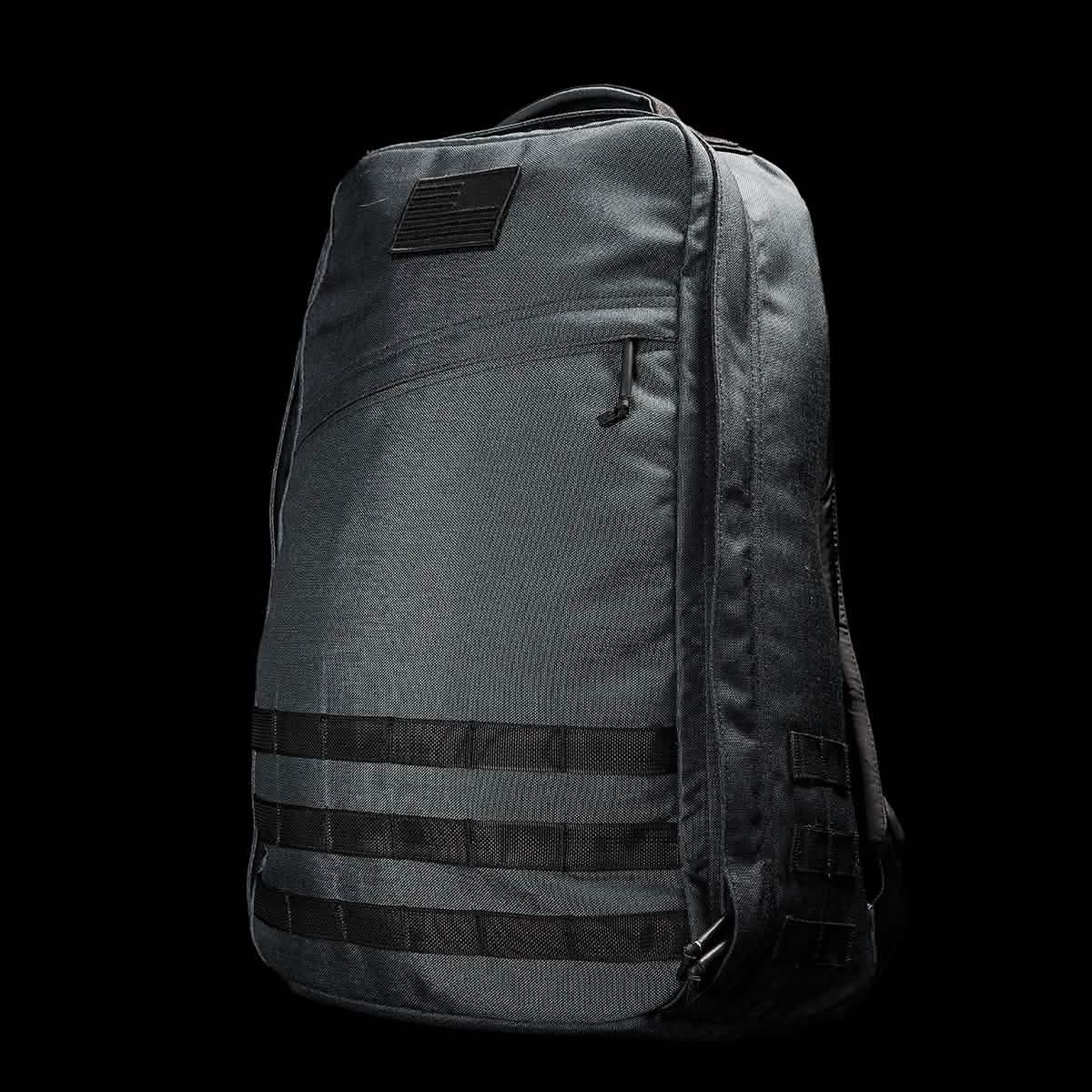 Introducing the GR1 USA - Cordura (The Original Ruck) by GORUCK: a rugged tactical backpack in black, designed with features reminiscent of the GORUCK Challenge. It sports horizontal strap loops on the front and a sleek silhouette, complete with a small patch at the top that enhances its Special Forces allure. The solid black background accentuates the texture and intricate details of the bag.