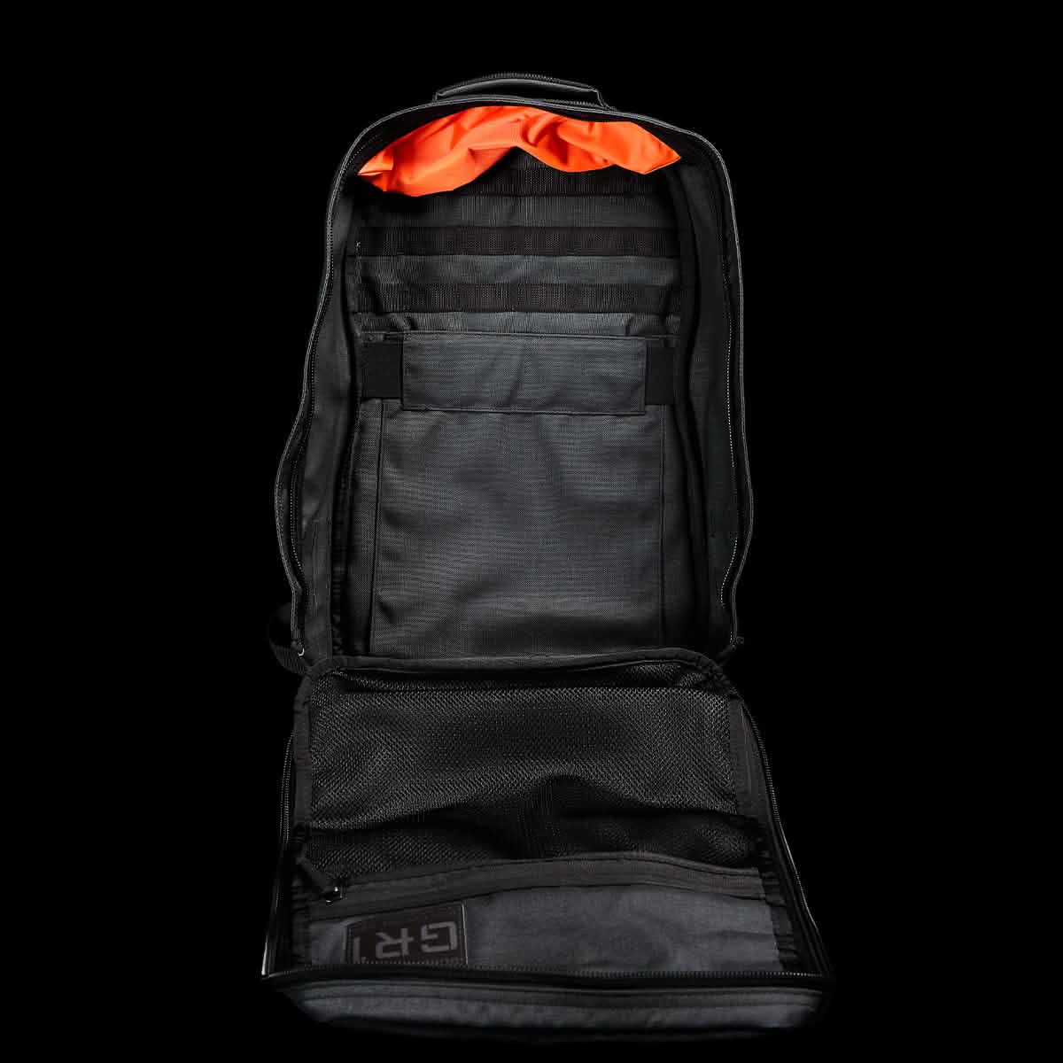 An open GR1 USA - Cordura (The Original Ruck) tactical backpack by GORUCK, showcasing its black exterior and multiple compartments with an orange interior lining, sits against a plain black background, poised for adventures reminiscent of a GORUCK Challenge.