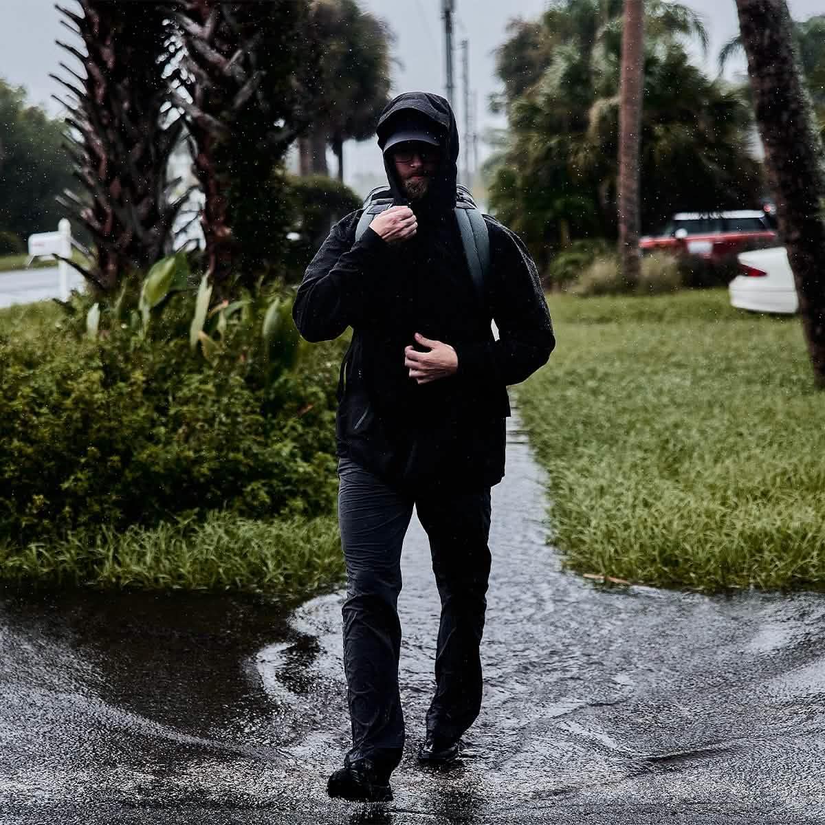 Person wearing black GORUCK gear and backpack walking through rain and puddles with palm trees in background