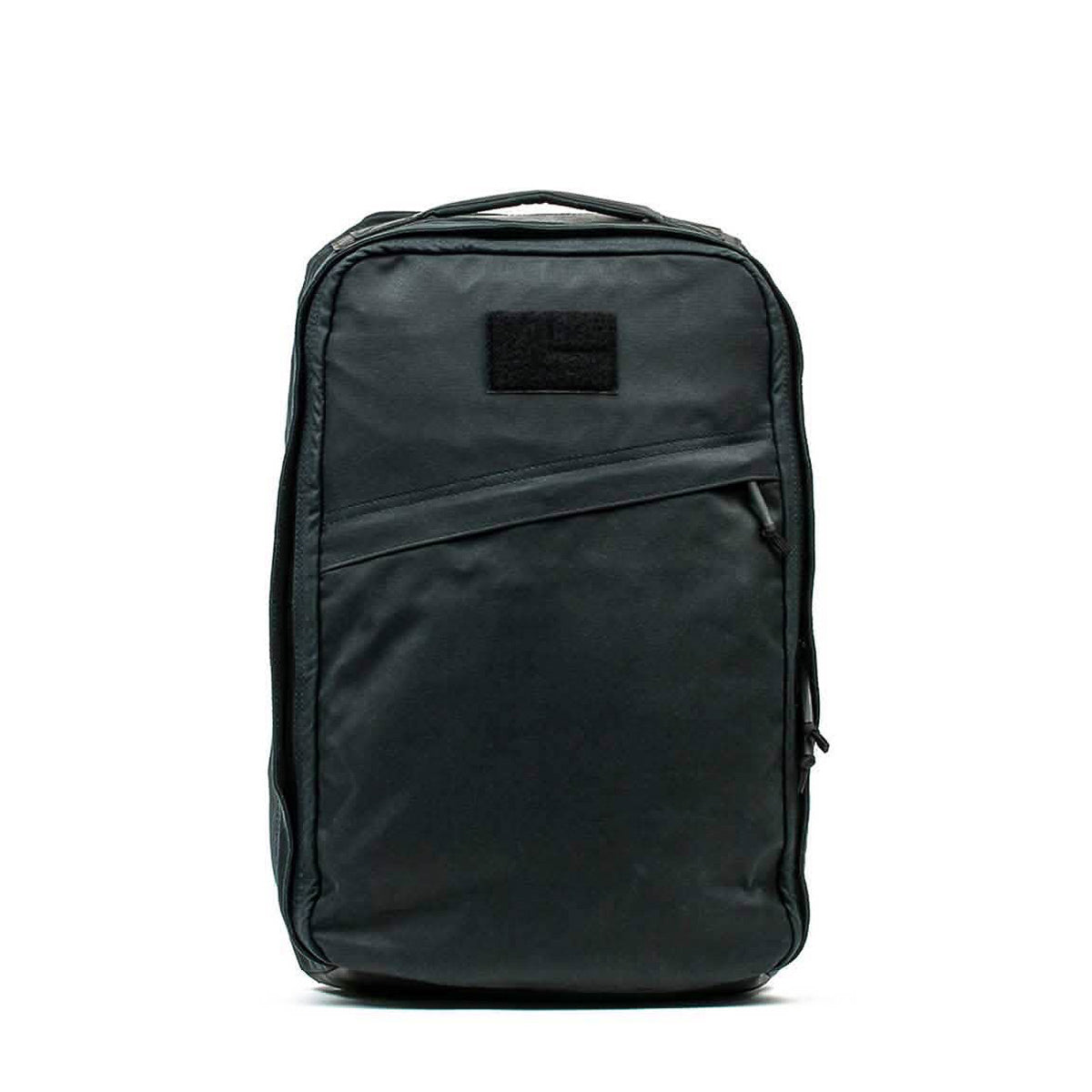The GR1 USA - Heritage Waxed Canvas is a black, rectangular backpack featuring a top handle and a front diagonal zipper pocket.