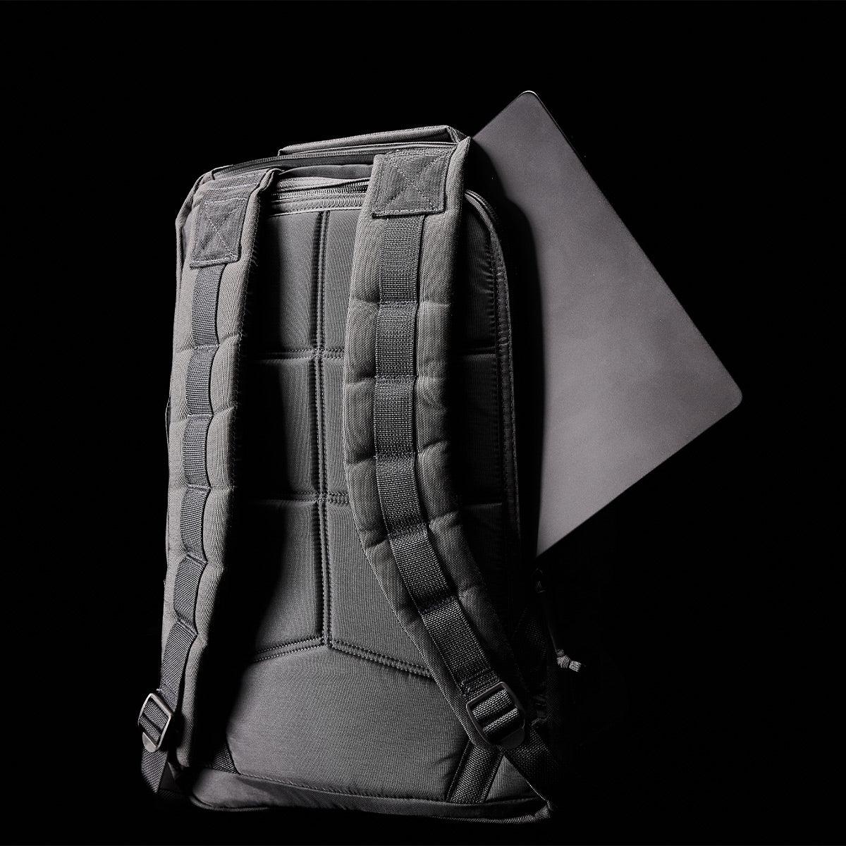 Back view of black GORUCK rucksack with padded straps and laptop partially inserted against black background