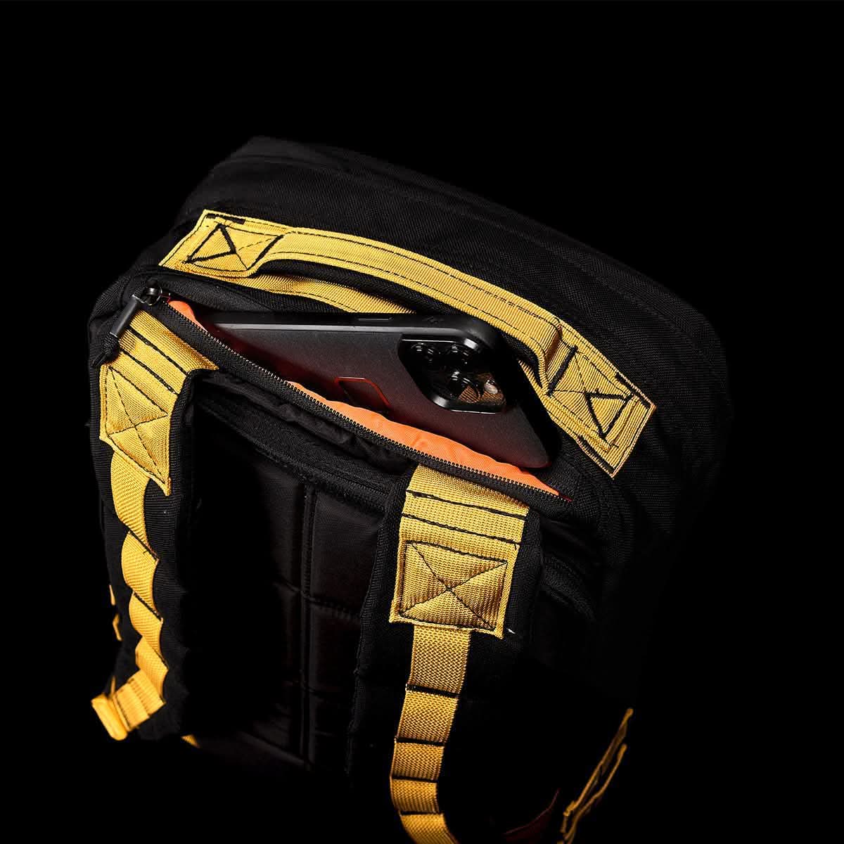 The GR1 USA - Cordura (The Original Ruck) from GORUCK, in a sleek black design, features eye-catching yellow straps. Partially open, it exposes a smartphone resting against the deep black interior, primed for any Special Forces-inspired adventure.