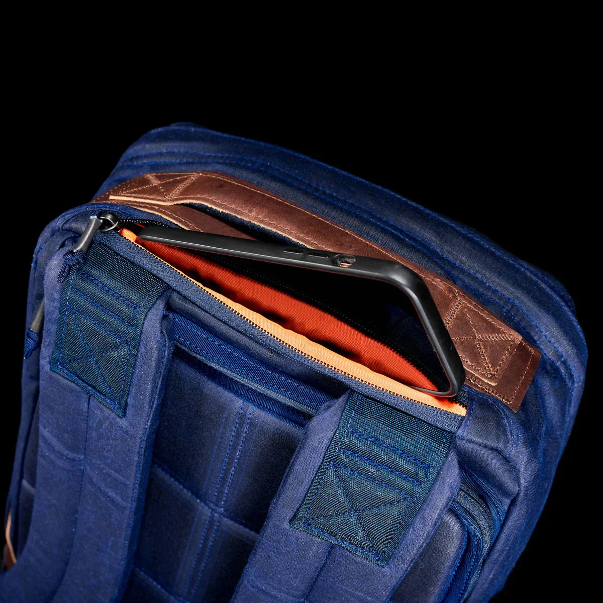 Close-up of navy GORUCK bag with padded straps, leather handle, and a smartphone in the back zipper pocket