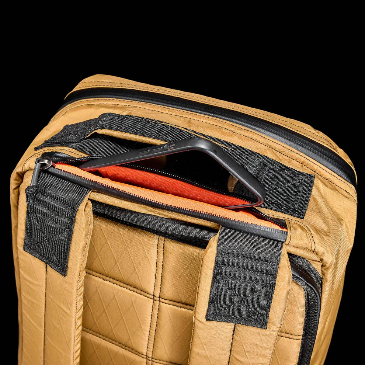 GORUCK GR1 26L backpack in coyote with padded back and zipped pocket holding a smartphone