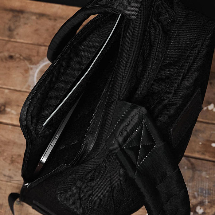 Black backpack on wooden floor with a laptop partially visible in the main compartment.