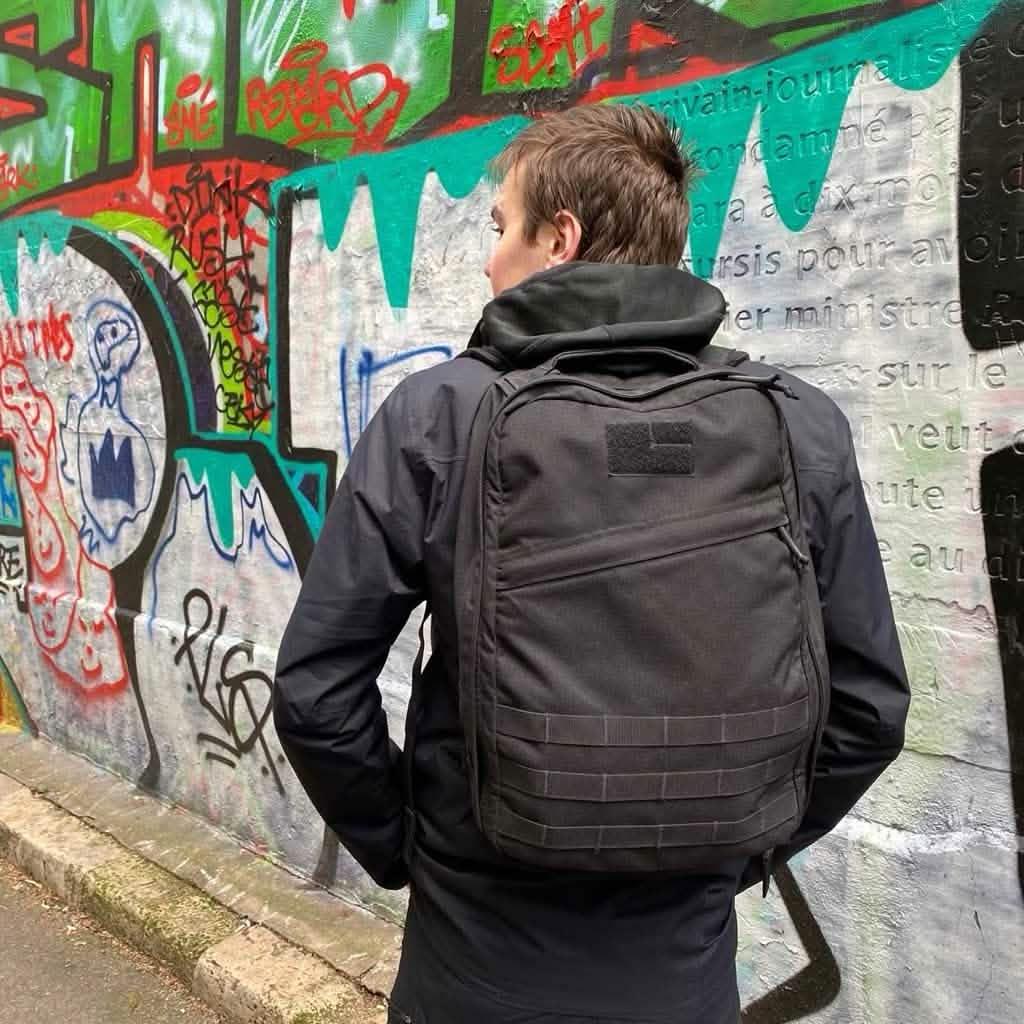 Person wearing a black GORUCK tactical backpack standing in front of a colorful graffiti wall