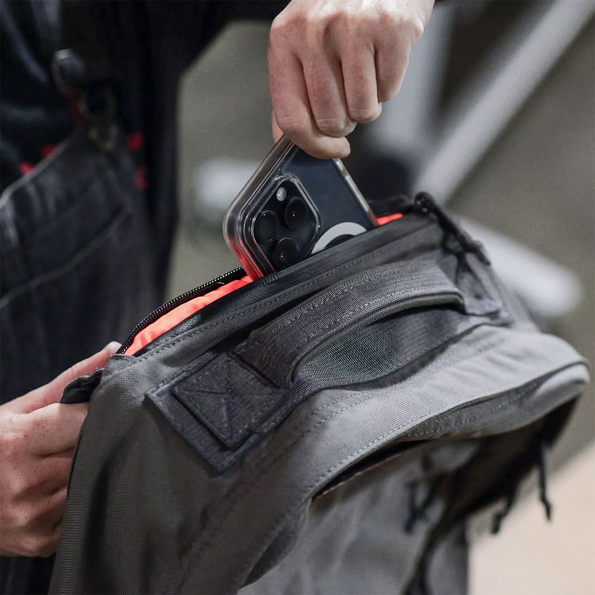 A person effortlessly slides their smartphone into the front pocket of the GR1 USA - Cordura rucksack by GORUCK, celebrated for its Special Forces-grade durability and bombproof laptop compartment.