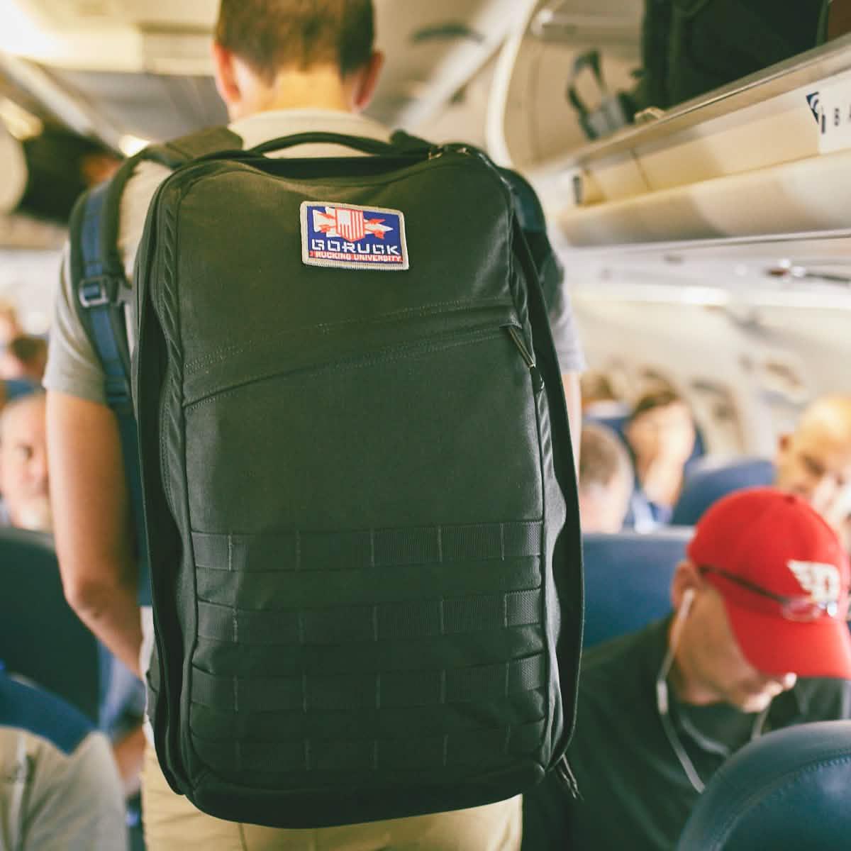 Person wearing a black GORUCK rucksack with patch inside an airplane cabin