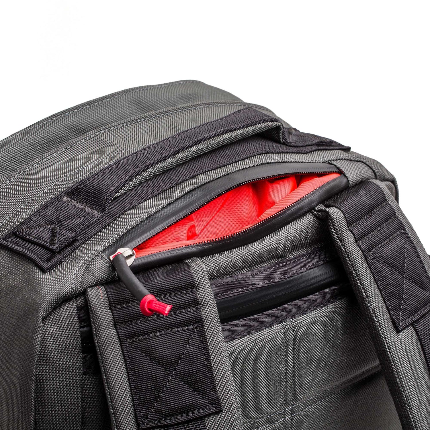 Close-up of a gray GR2 - Cordura ruck with an unzipped pocket, showing its bright red interior lining.