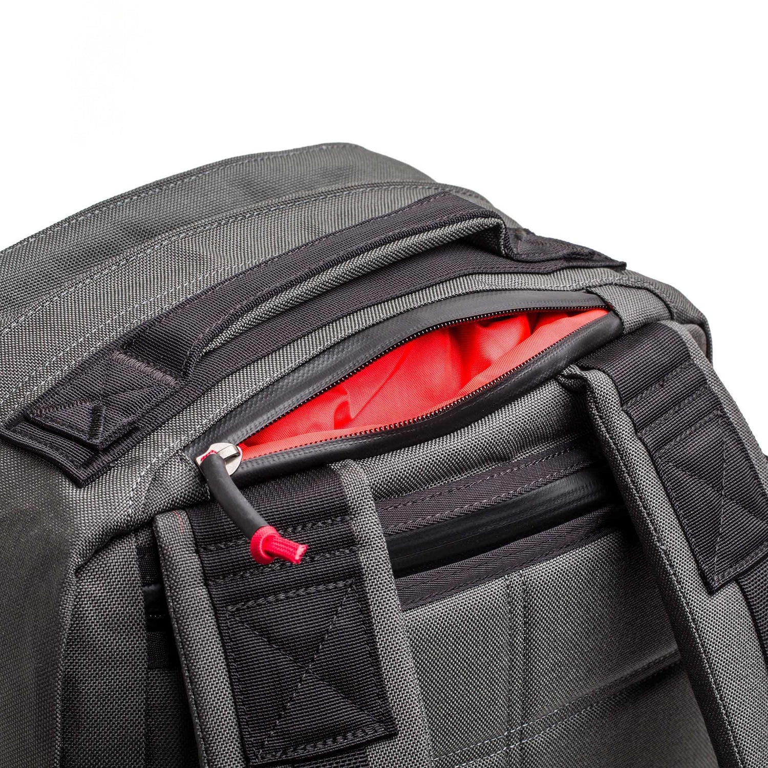 Close-up of a gray GR2 - Cordura ruck with an unzipped pocket, showing its bright red interior lining.