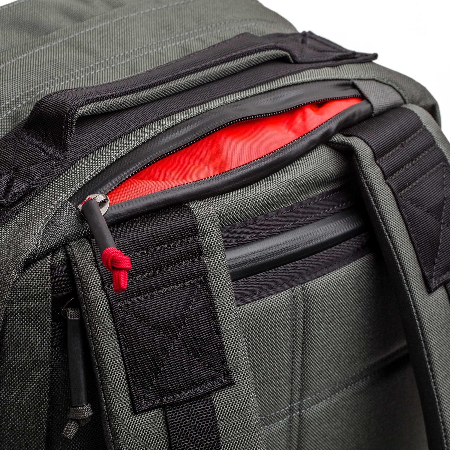A close-up of the gray GR2 - Cordura backpack, featuring black zippers and a red interior, partially unzipped at the top.