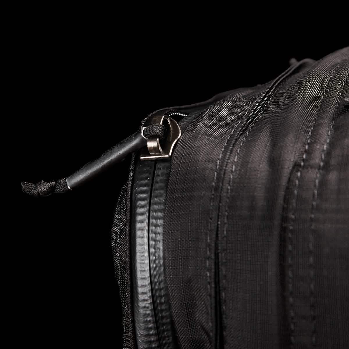 Close-up of the GR2 - Ripstop ROBIC® travel bag by GORUCK, featuring a slightly open zipper with a black cord attached to the pull. The fabric texture and stitching stand out against the dark background, emphasizing its water-resistant design.
