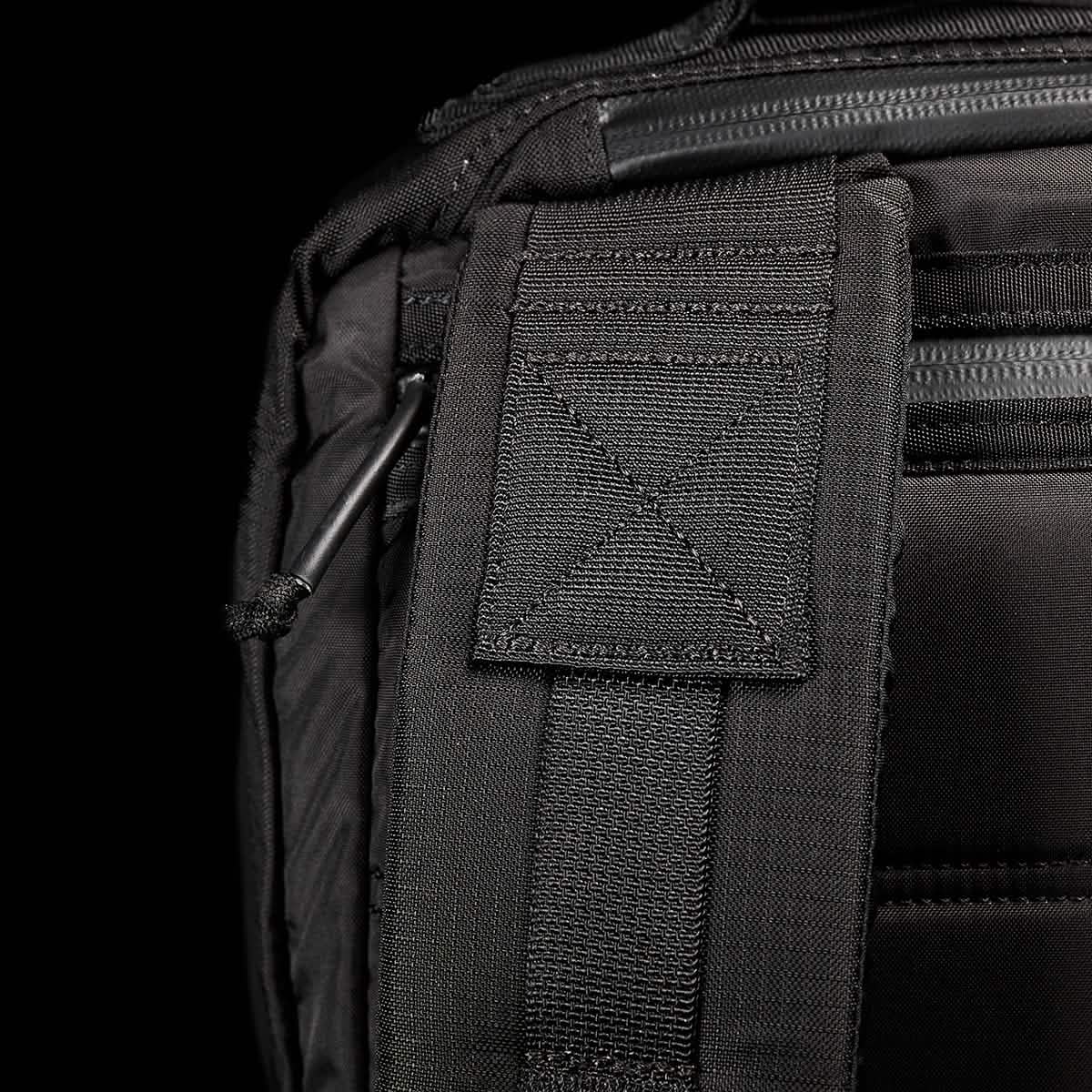 Close-up of the GR2 - Ripstop ROBIC® rucksack by GORUCK displaying detailed stitching and a padded strap. The texture of the fabric stands out, highlighting its water-resistant quality, with a partially visible metal clip. The dark background underscores the premium design and craftsmanship of this black travel bag.