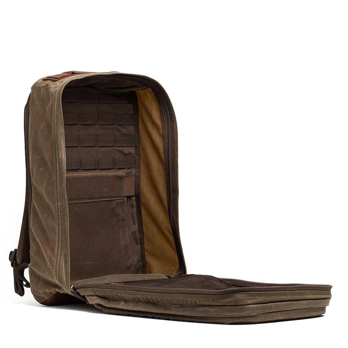 Open dark oak GORUCK rucksack with organized interior pockets and MOLLE webbing on white background