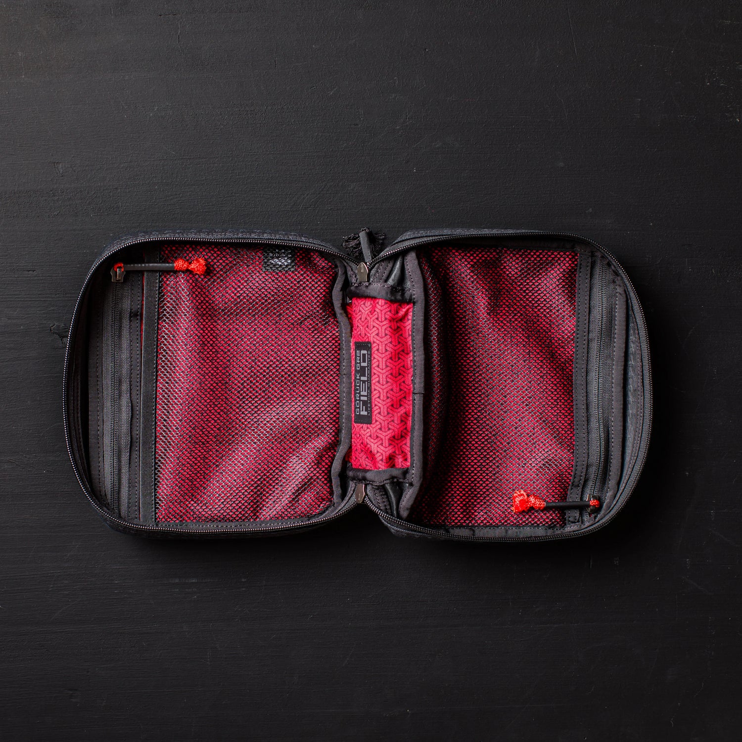 Open GORUCK Field Pocket with red interior mesh pockets and black zippers on dark surface