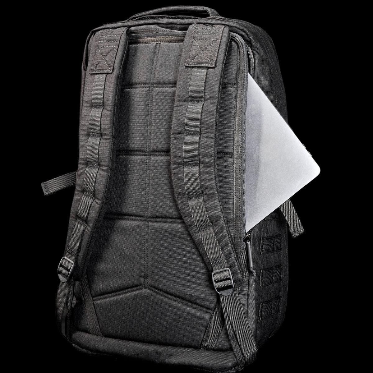Black GORUCK backpack with padded back and shoulder straps, partially open showing silver laptop inside