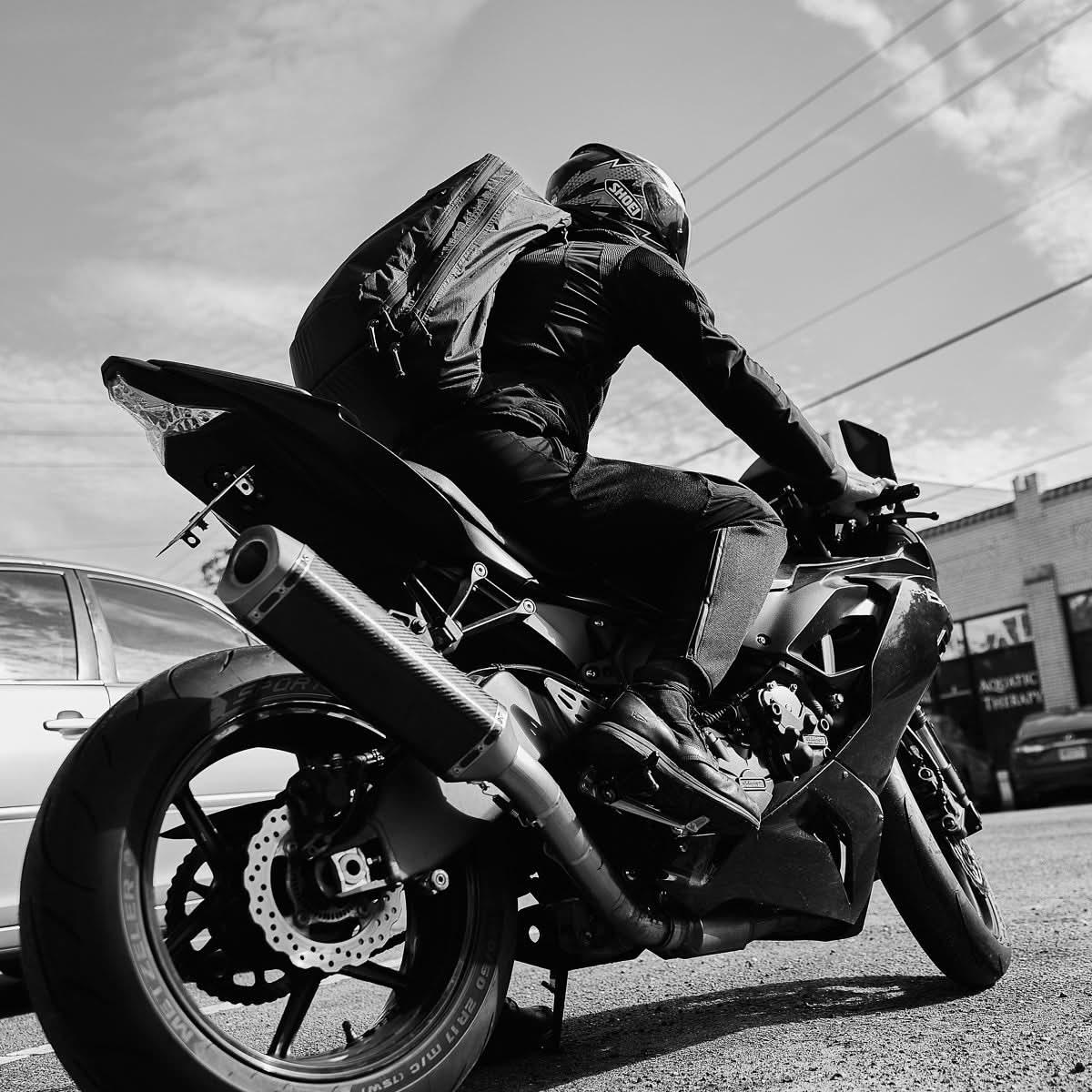 Motorcyclist wearing GORUCK rucksack rides street bike, showcasing rugged rucking gear.