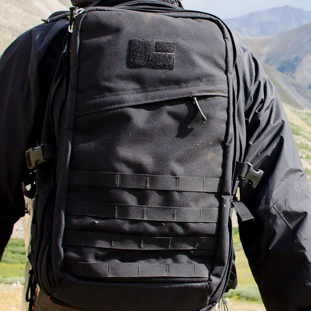 Close-up of a black GORUCK rucksack worn on a person hiking in mountainous terrain