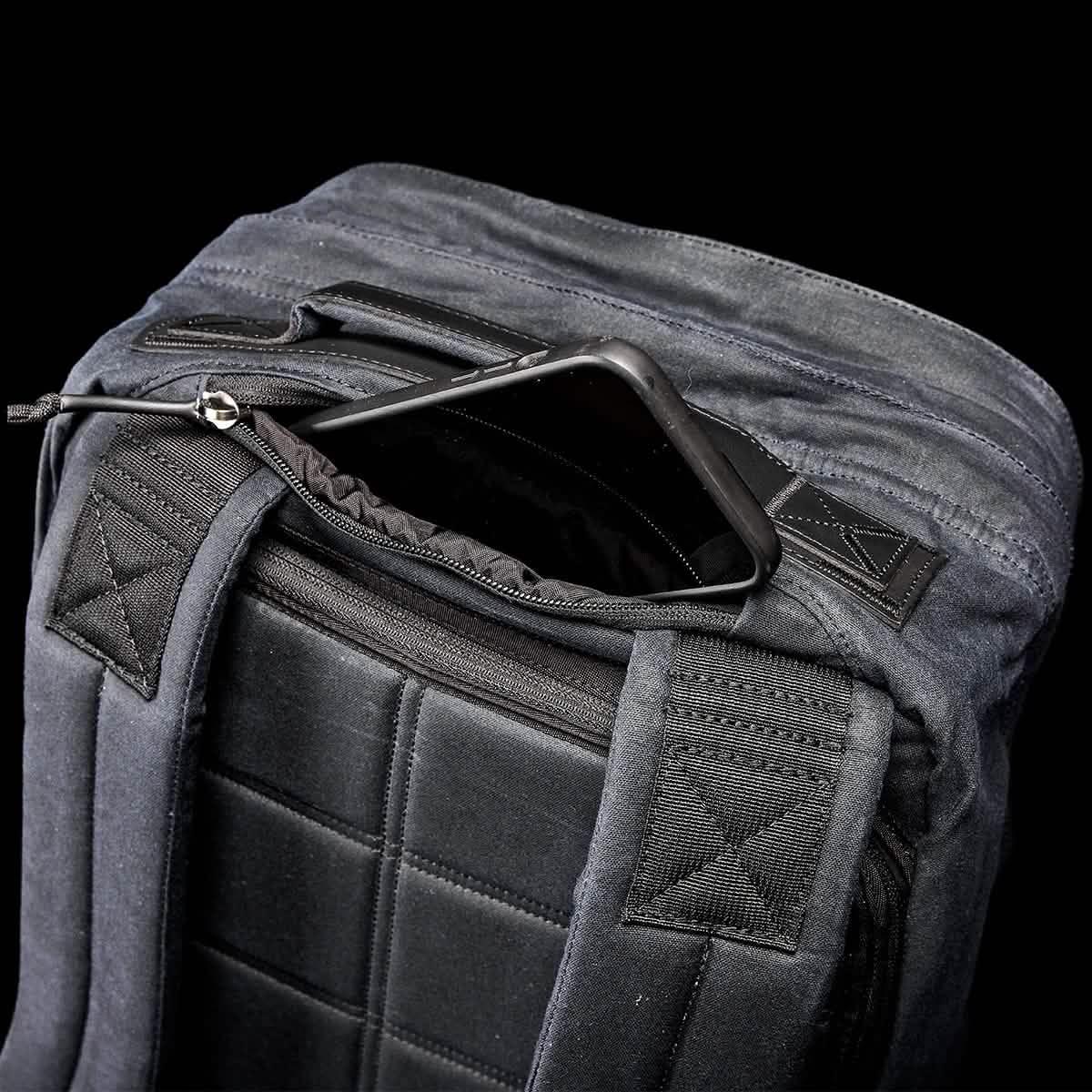 A top view of the GR2 - Waxed Canvas by GORUCK showcases its black exterior, padded straps, and an open main compartment with a smartphone partially tucked inside. The back features a textured, quilted design that exudes classic elegance.