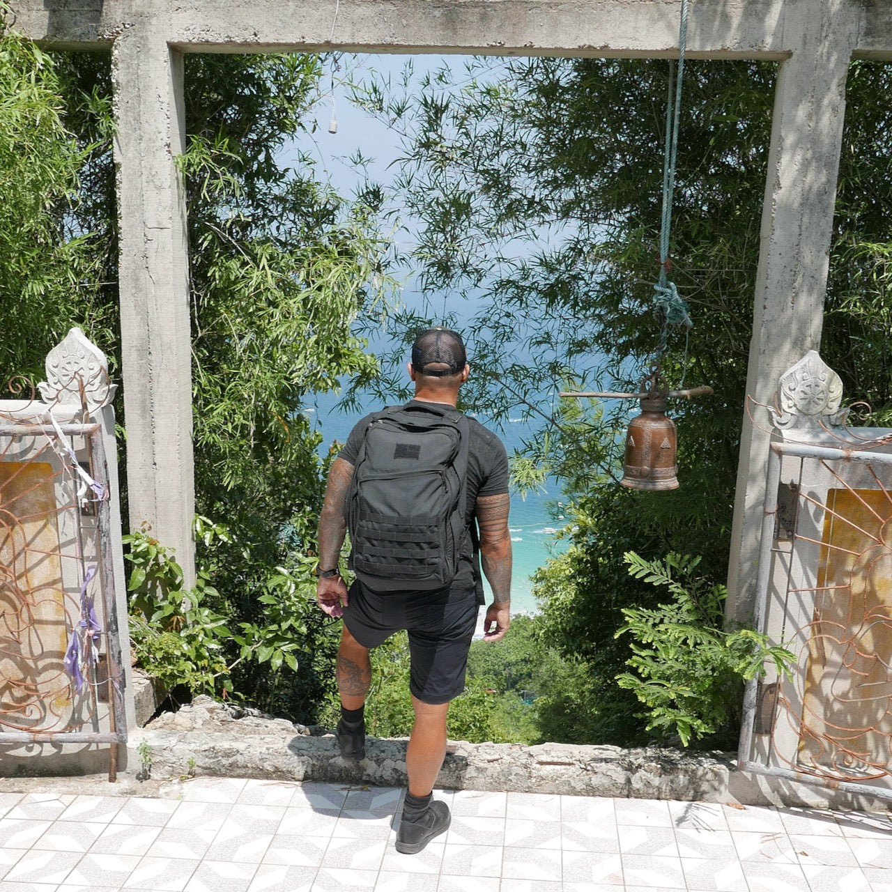 A person with a GR2 USA - Cordura rucksack stands at a stone frame, overlooking lush greenery and the ocean below.