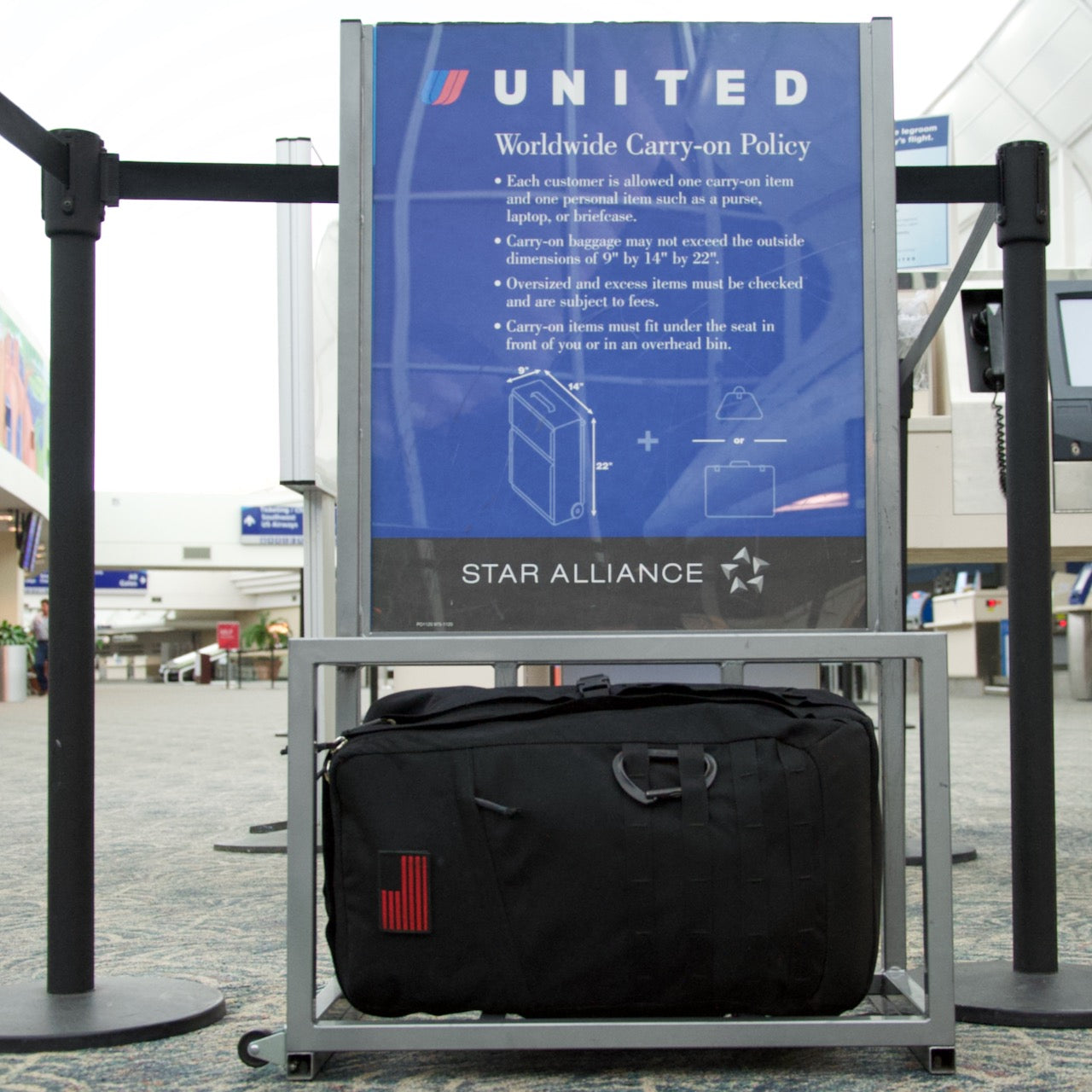 A GR2 USA - Cordura black travel backpack under a United Airlines baggage size checker at an airport.