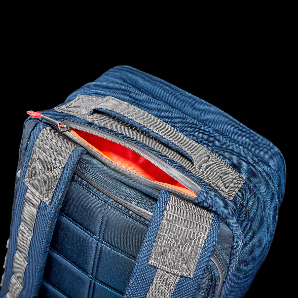 A close-up of the GR2 - Cordura ruck shows off its rugged design, with a partially open zipper revealing a vibrant orange interior against a stark black background.