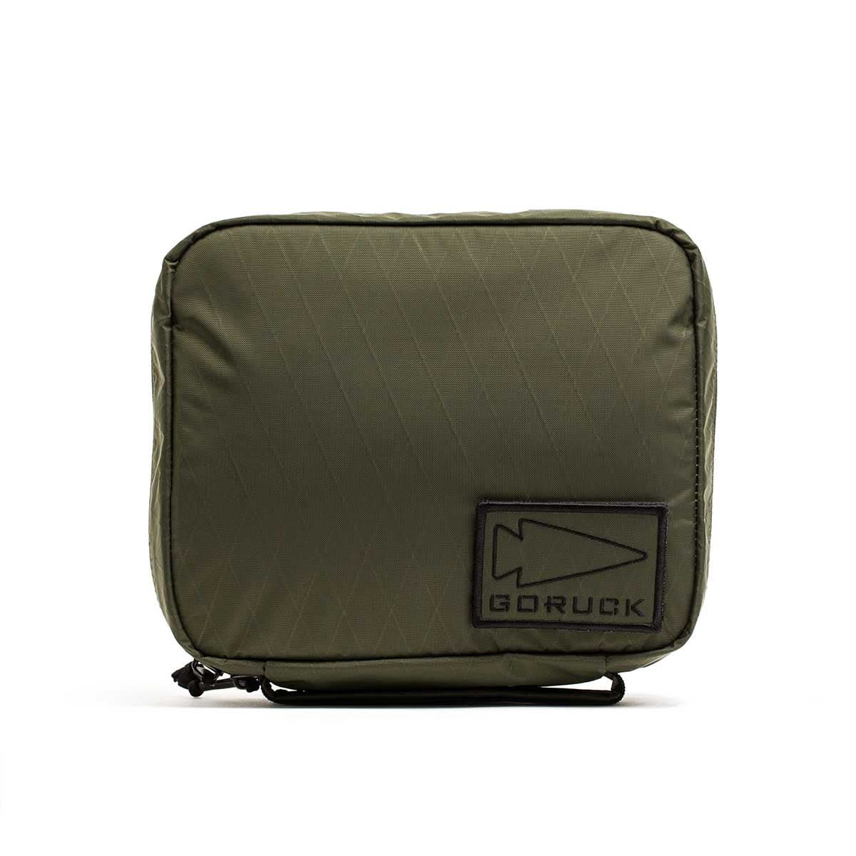 The GR2 Field Pocket - X-PAC is an olive green electronics organizer pouch with a black arrowhead logo patch on the front, made from waterproof fabric and shown against a white background.