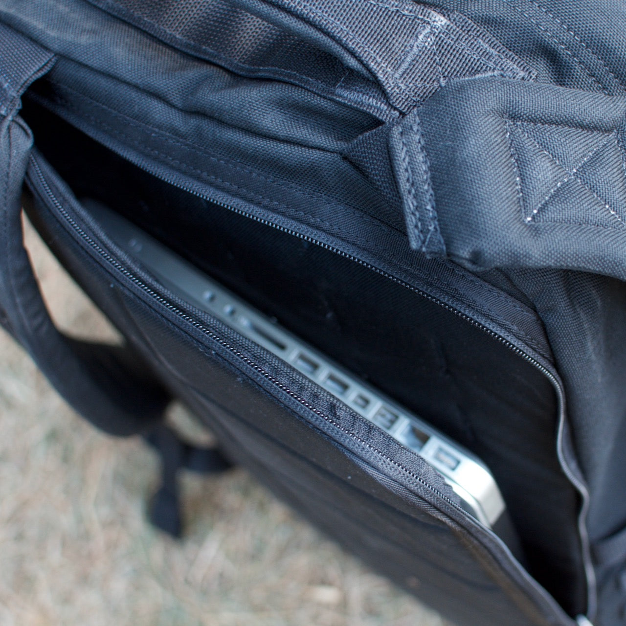 A silver laptop is partially visible inside the front zippered pocket of a black GR2 USA - Cordura backpack.