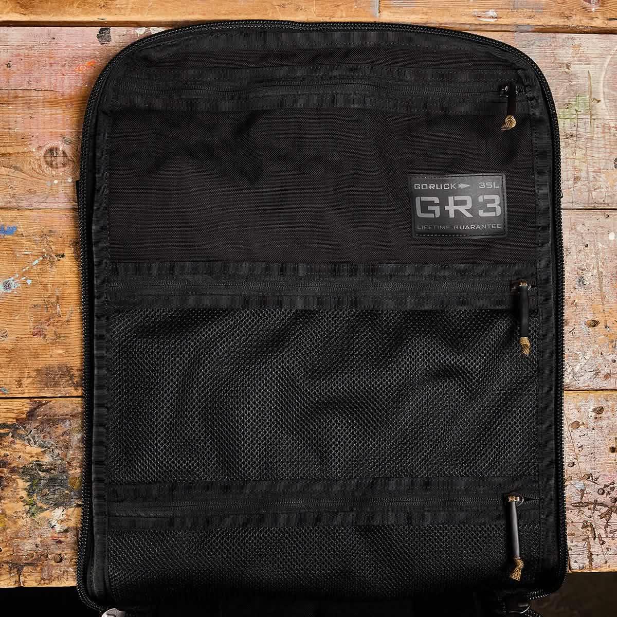 GORUCK GR3 35L rucksack in black, open on rustic wooden surface, mesh organizer pockets visible