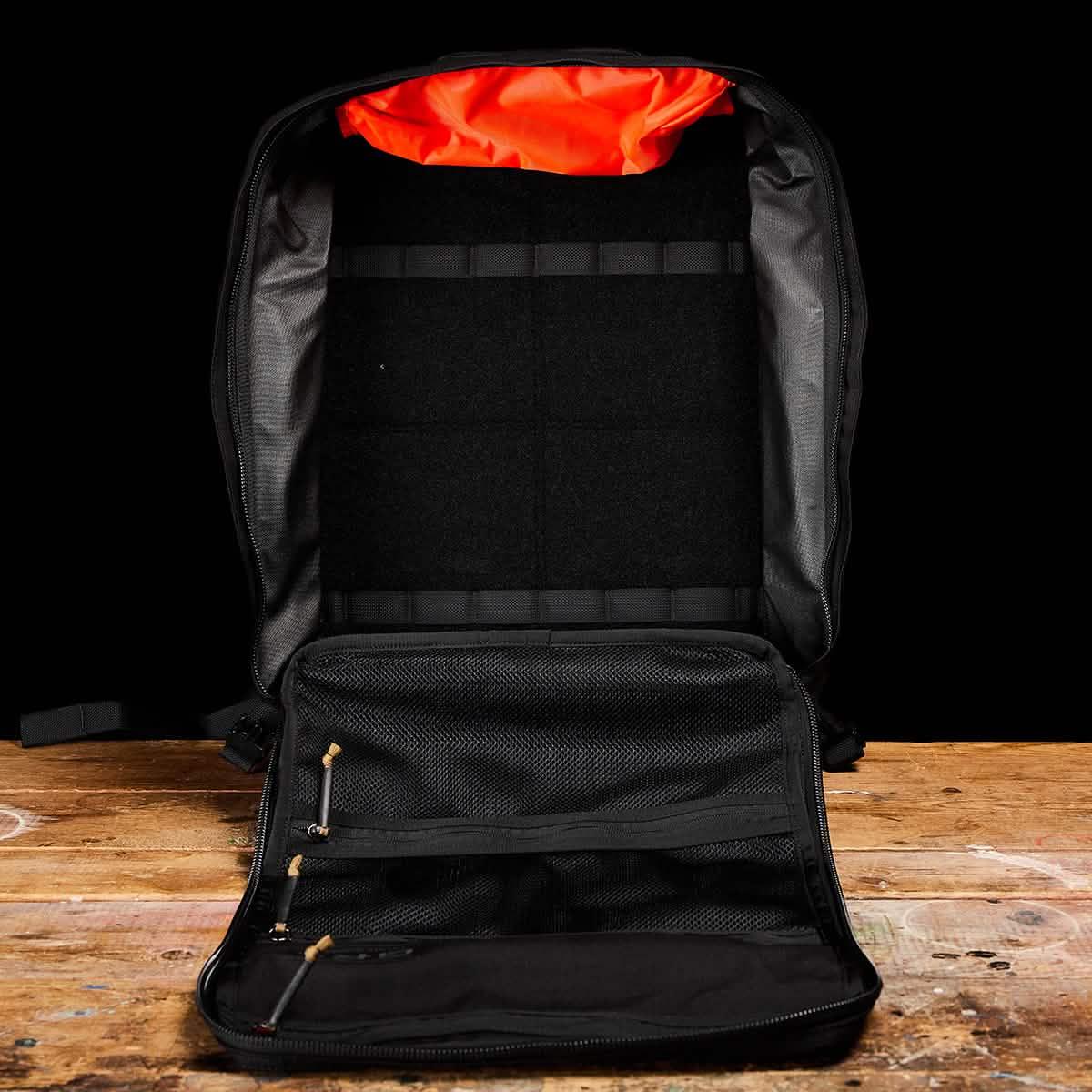Open black GORUCK backpack with orange interior pocket on wooden surface, showcasing durable rucking gear design