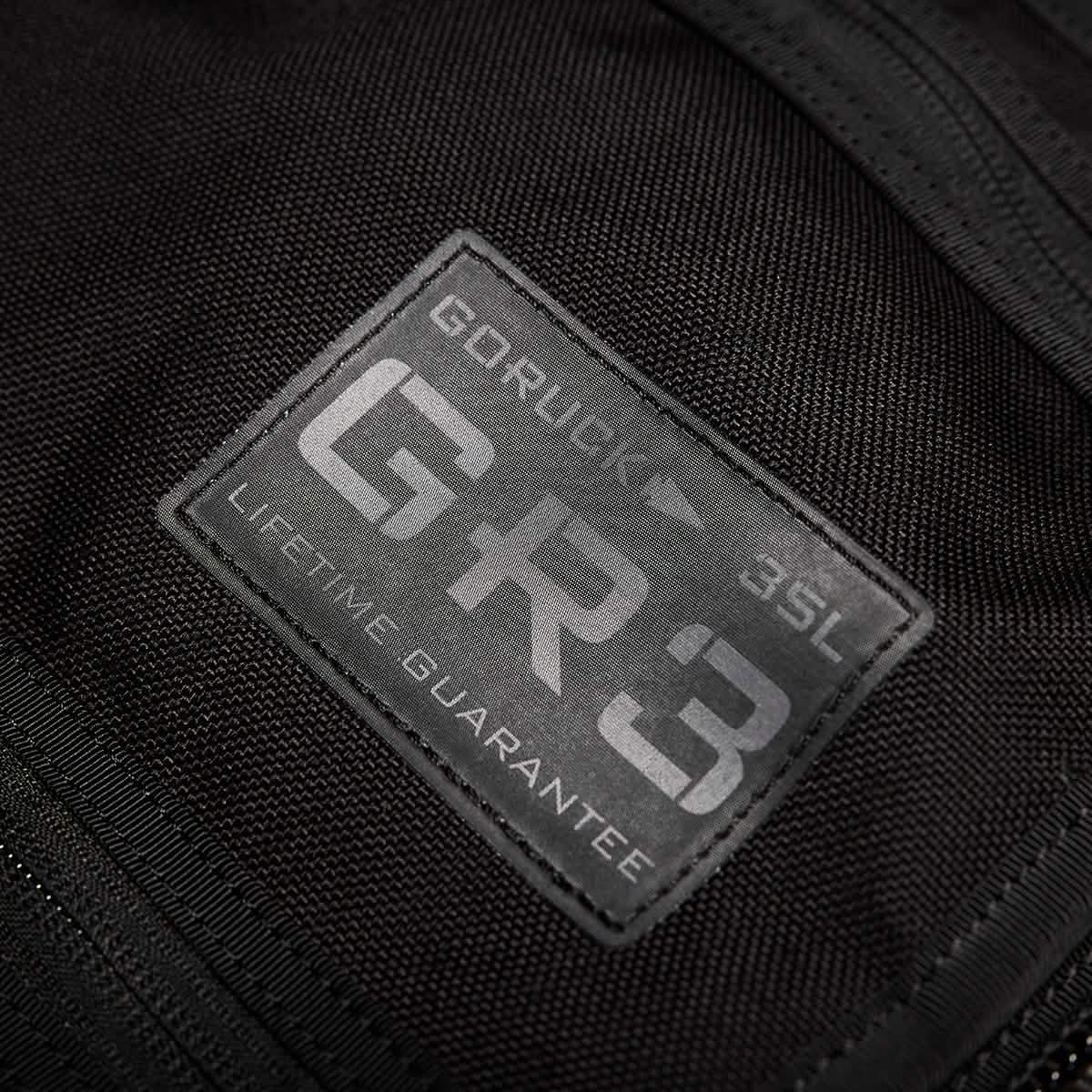 Close-up of a black fabric patch on a carry-on rucksack displaying the text: GORUCK - GR3® - Cordura LIFETIME GUARANTEE. The rugged, water-resistant patch is stitched onto the fabric, highlighting durability and quality.