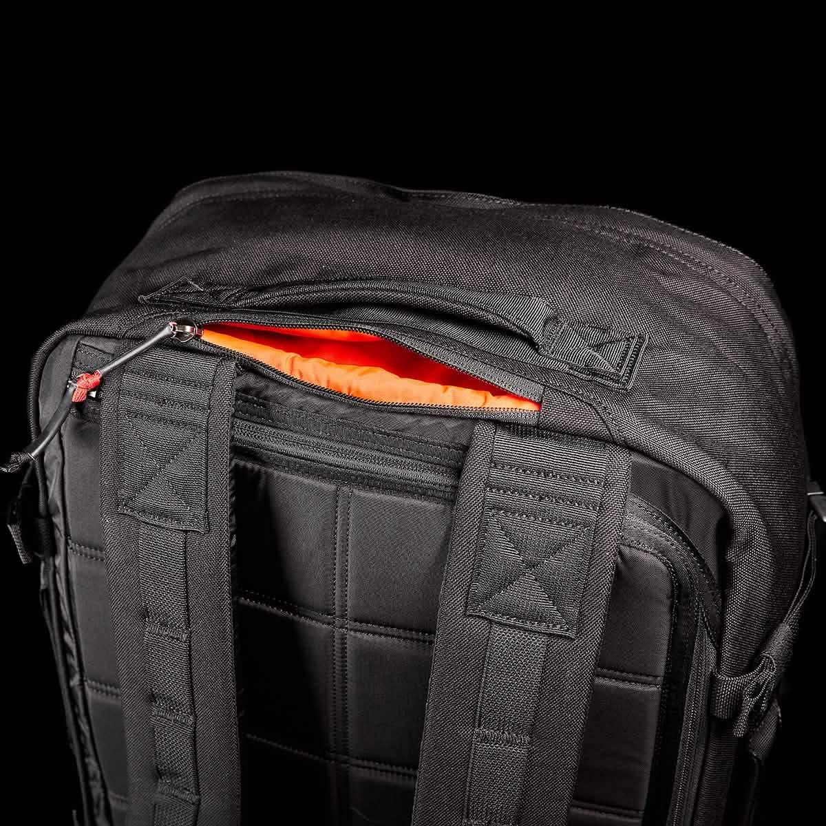 Close-up of black GORUCK rucksack showing padded back, shoulder straps, and partially opened zipper with orange interior