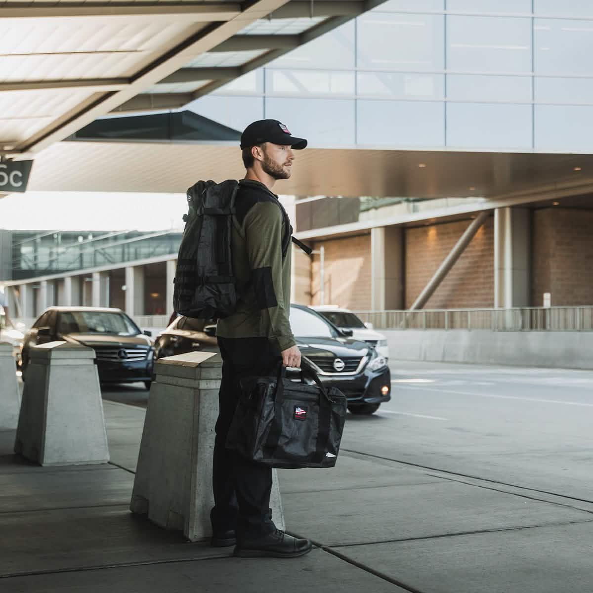 Man at airport curb with GORUCK black rucksack and duffel bag, ready for travel